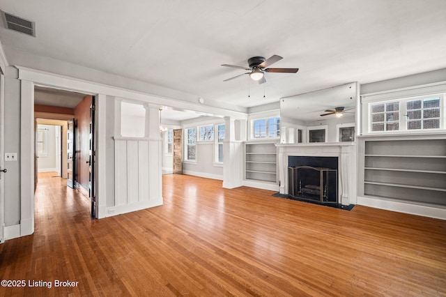 unfurnished living room featuring visible vents, baseboards, a ceiling fan, a fireplace with flush hearth, and wood finished floors