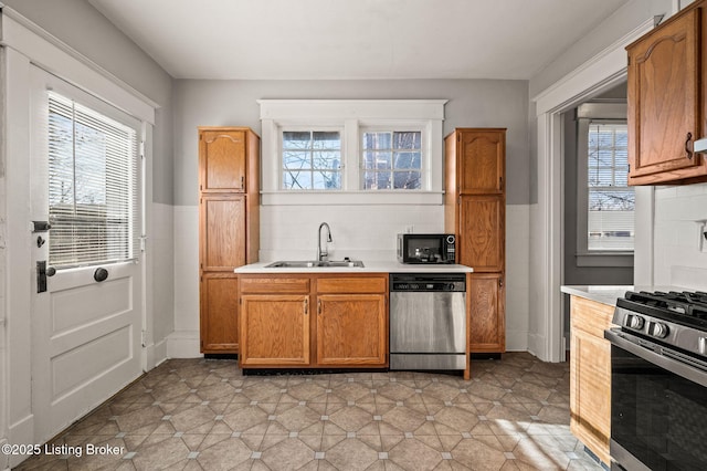 kitchen featuring stainless steel appliances, wainscoting, a sink, and light countertops