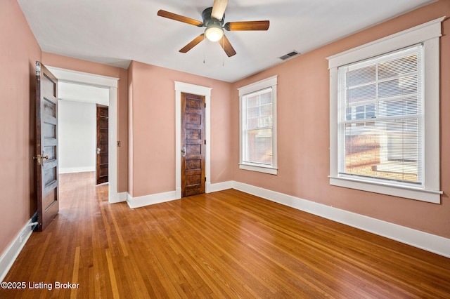 spare room featuring a ceiling fan, visible vents, baseboards, and wood finished floors