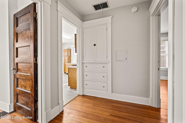 hallway featuring visible vents, baseboards, and wood finished floors