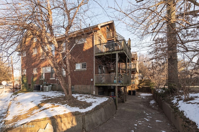 snow covered property with stairway, central AC unit, and brick siding