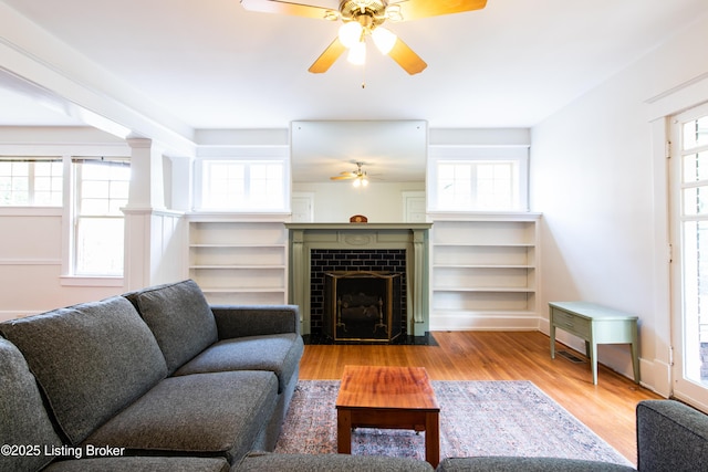 living room with a tiled fireplace, a ceiling fan, and wood finished floors