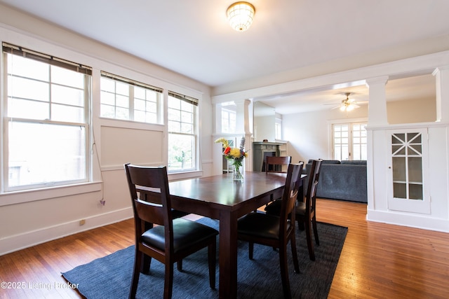 dining space with baseboards, ceiling fan, wood finished floors, ornate columns, and a fireplace