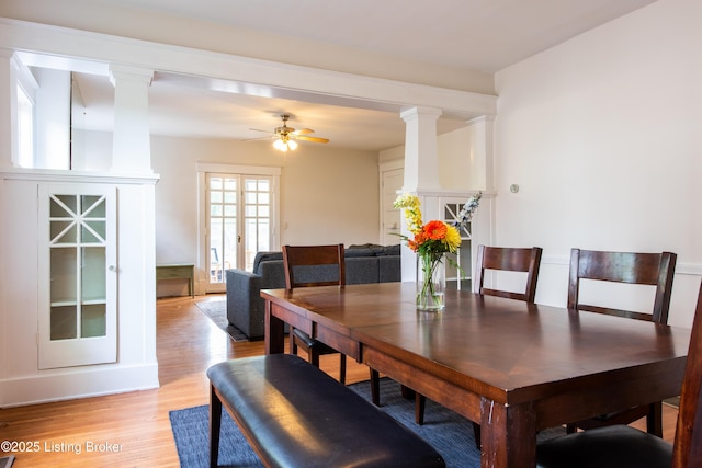 dining area with light wood-type flooring, decorative columns, and a ceiling fan