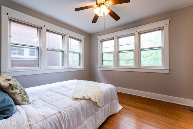 bedroom featuring a ceiling fan, visible vents, baseboards, and wood finished floors