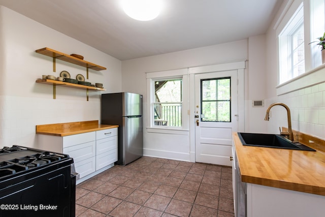 kitchen with black range with gas cooktop, butcher block counters, freestanding refrigerator, open shelves, and a sink