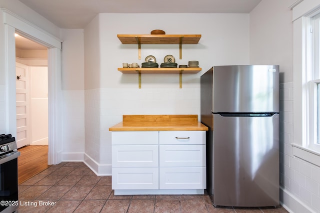 kitchen with tile walls, stainless steel appliances, wooden counters, wainscoting, and white cabinets