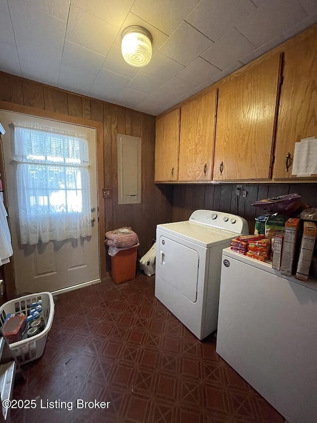 laundry area with cabinets, electric panel, wooden walls, and washing machine and clothes dryer