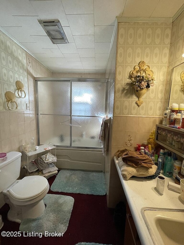 full bathroom featuring tile walls, combined bath / shower with glass door, ornamental molding, and toilet