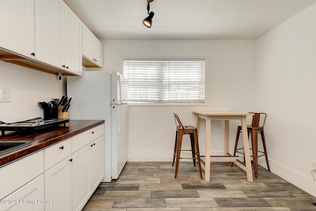 kitchen with hardwood / wood-style floors, white cabinetry, white refrigerator, butcher block counters, and rail lighting