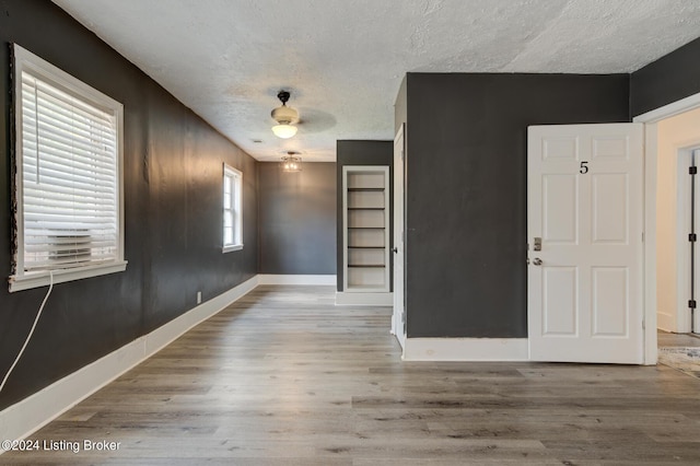 empty room featuring light wood-type flooring, built in features, and a textured ceiling