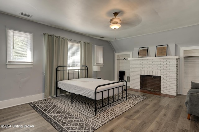 bedroom featuring ceiling fan, a fireplace, hardwood / wood-style flooring, and multiple windows