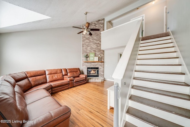 living room with hardwood / wood-style floors, a fireplace, lofted ceiling, ceiling fan, and a textured ceiling