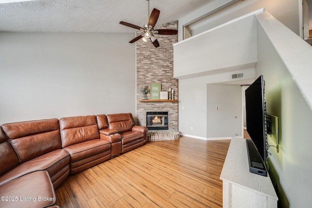 living room with high vaulted ceiling, ceiling fan, light hardwood / wood-style floors, a brick fireplace, and a textured ceiling