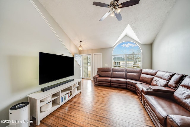 living room with lofted ceiling, ceiling fan, a textured ceiling, and light wood-type flooring