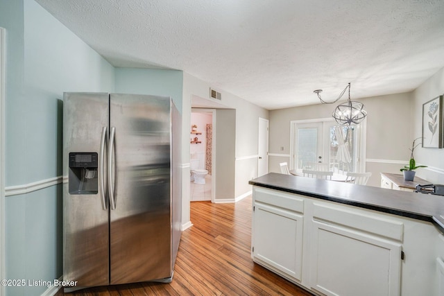 kitchen with stainless steel refrigerator with ice dispenser, light hardwood / wood-style floors, a textured ceiling, white cabinets, and decorative light fixtures