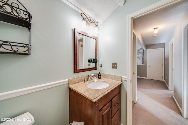 bathroom with toilet, vaulted ceiling, a textured ceiling, ornamental molding, and vanity