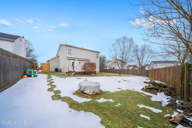 snow covered back of property with a yard, central AC, and a deck