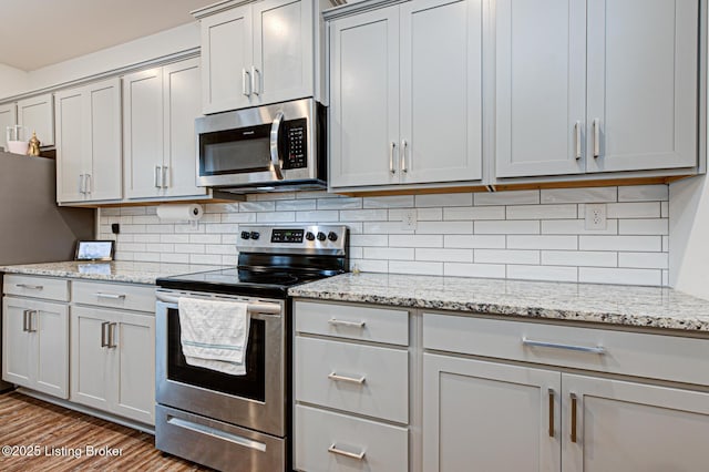 kitchen with stainless steel appliances, light stone countertops, light wood-type flooring, and decorative backsplash