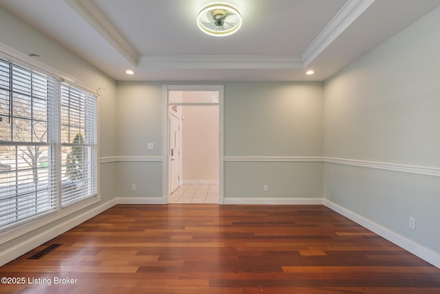 empty room featuring a tray ceiling, visible vents, ornamental molding, wood finished floors, and baseboards