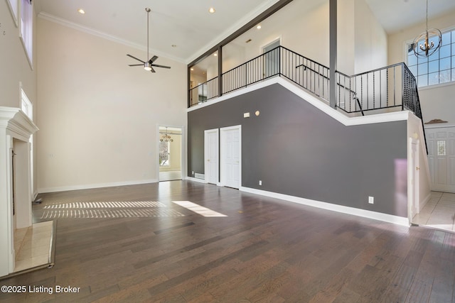 unfurnished living room featuring a high ceiling, ornamental molding, ceiling fan with notable chandelier, and dark hardwood / wood-style flooring