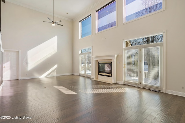 unfurnished living room featuring ceiling fan, a towering ceiling, dark hardwood / wood-style floors, a fireplace, and ornamental molding