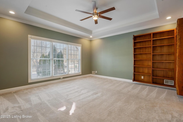 unfurnished room featuring a raised ceiling, ornamental molding, light carpet, and ceiling fan