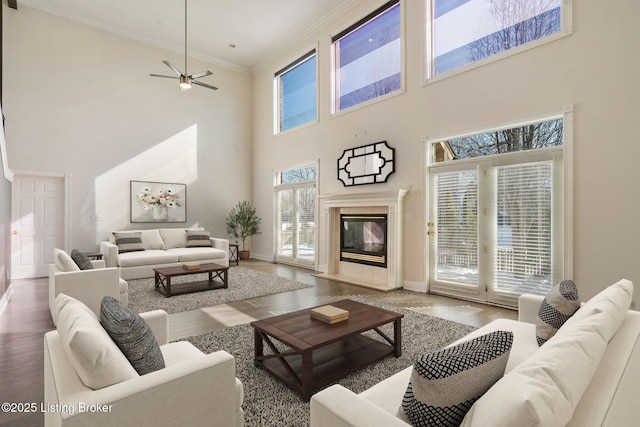 living room featuring ceiling fan, a fireplace, wood finished floors, baseboards, and crown molding