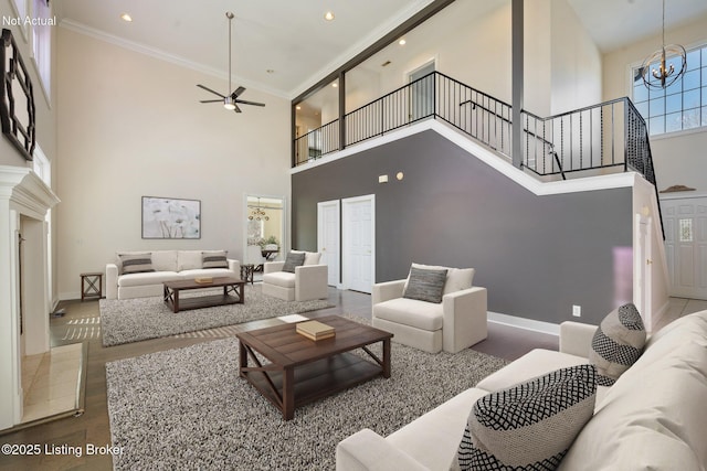 living room with ceiling fan with notable chandelier, ornamental molding, hardwood / wood-style floors, and a high ceiling