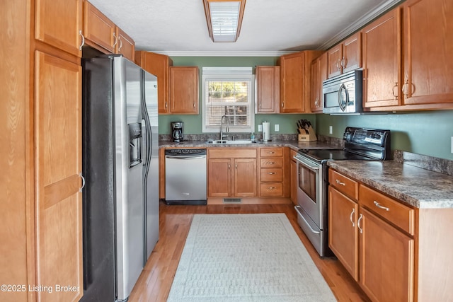 kitchen featuring sink, appliances with stainless steel finishes, light hardwood / wood-style flooring, and ornamental molding