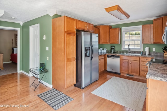 kitchen featuring a textured ceiling, stainless steel appliances, sink, ornamental molding, and light wood-type flooring