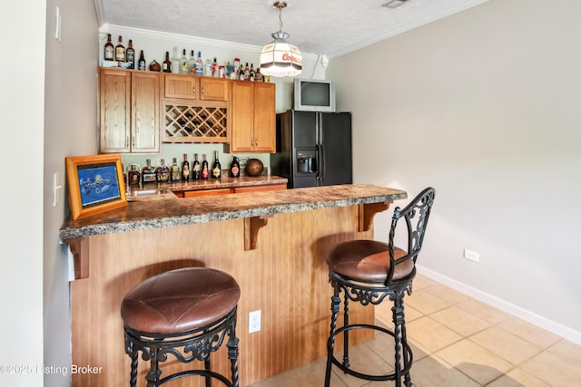 bar with decorative light fixtures, black refrigerator with ice dispenser, light tile patterned flooring, a textured ceiling, and ornamental molding