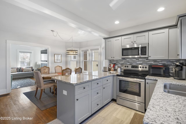 kitchen featuring hanging light fixtures, stainless steel appliances, light stone countertops, decorative backsplash, and kitchen peninsula