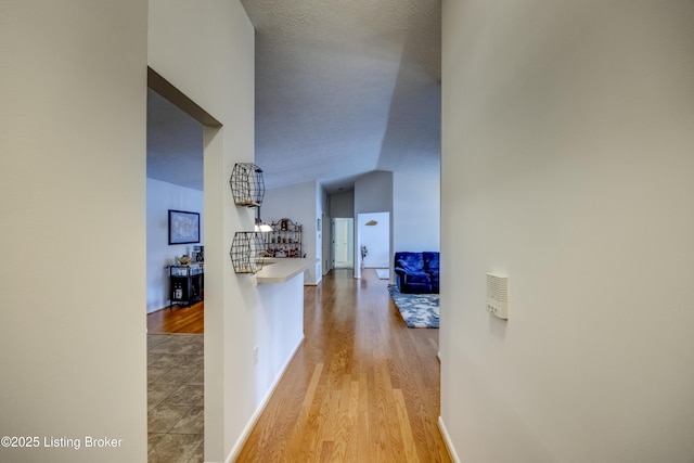 hallway with vaulted ceiling, a textured ceiling, and light hardwood / wood-style flooring