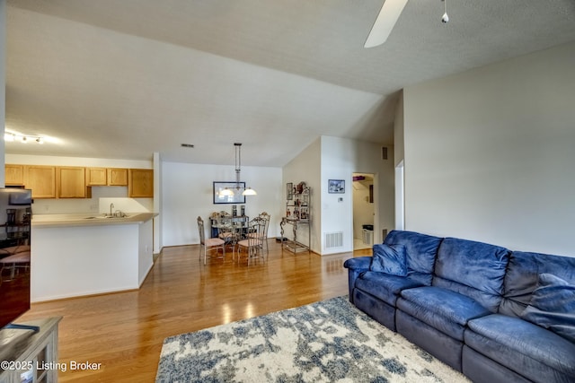 living room featuring vaulted ceiling, ceiling fan, sink, and light hardwood / wood-style flooring