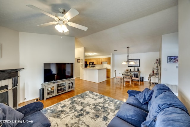 living room featuring ceiling fan, lofted ceiling, a fireplace, and light wood-type flooring