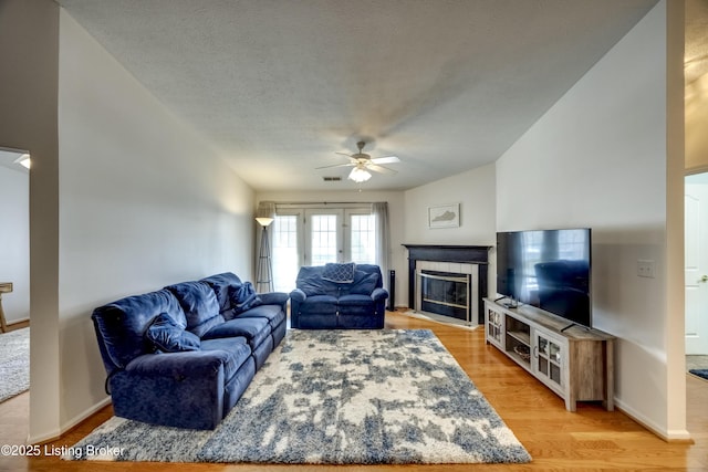 living room with ceiling fan, wood-type flooring, a tile fireplace, and a textured ceiling