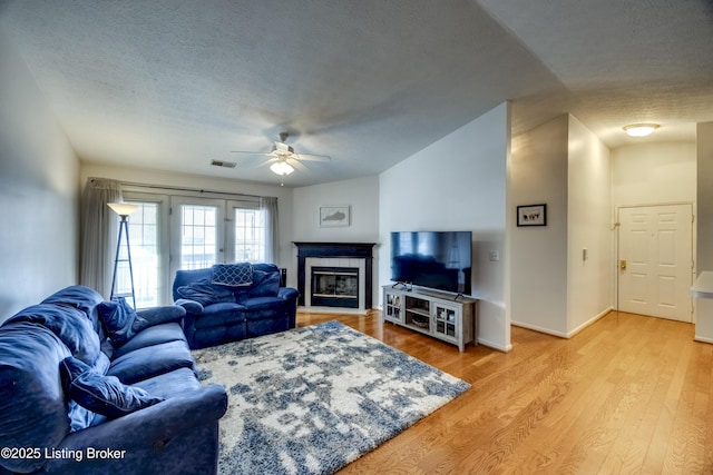 living room featuring ceiling fan, light hardwood / wood-style flooring, a tile fireplace, and a textured ceiling