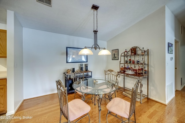 dining area with vaulted ceiling, an inviting chandelier, and light hardwood / wood-style floors