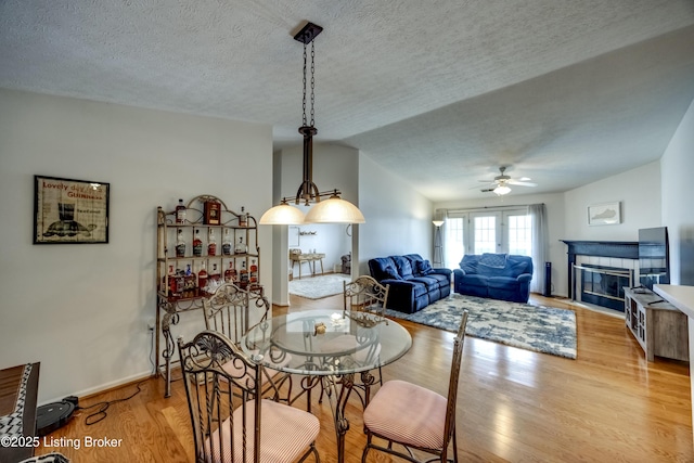 dining room with lofted ceiling, light hardwood / wood-style flooring, a textured ceiling, ceiling fan, and a fireplace