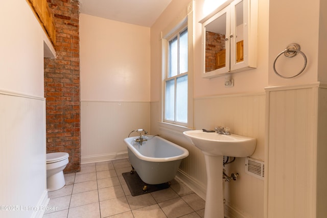 bathroom with tile patterned floors, a bath, toilet, and a healthy amount of sunlight