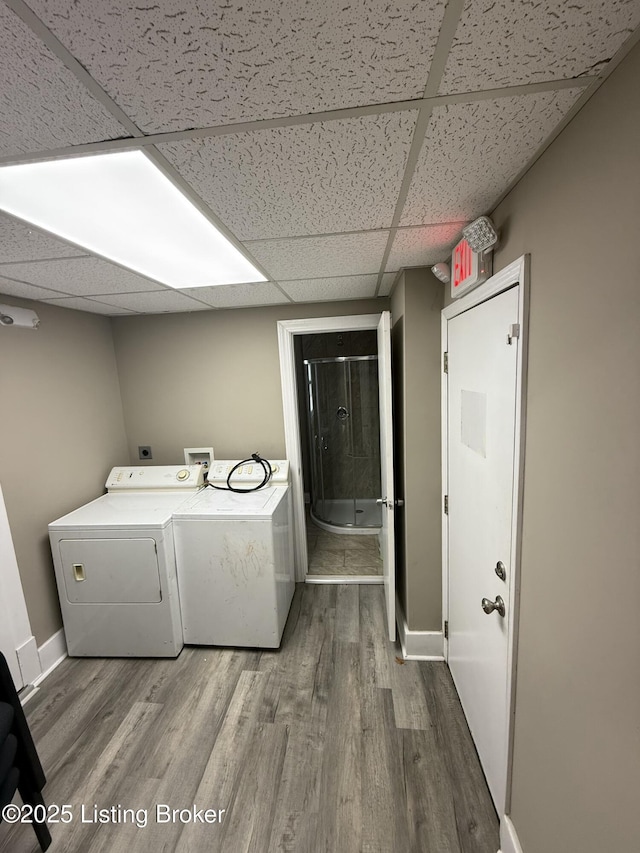 clothes washing area featuring washing machine and clothes dryer, laundry area, baseboards, and wood finished floors