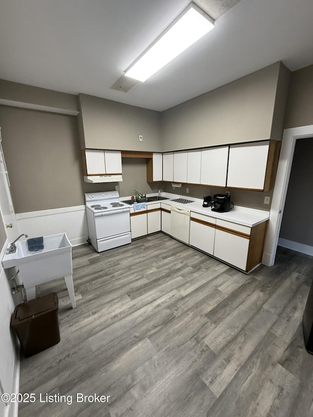 kitchen featuring wood finished floors, white appliances, white cabinetry, and a sink