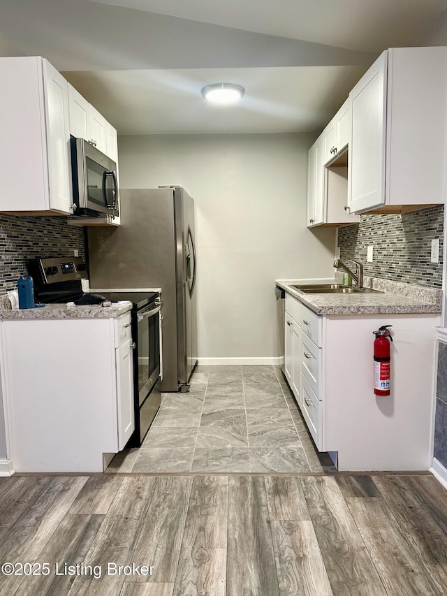 kitchen featuring stainless steel appliances, tasteful backsplash, lofted ceiling, white cabinets, and sink