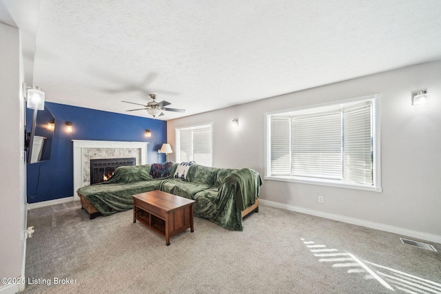 carpeted living room with ceiling fan, a textured ceiling, and a tiled fireplace