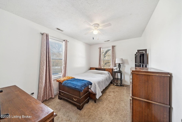 carpeted bedroom featuring ceiling fan, multiple windows, and a textured ceiling