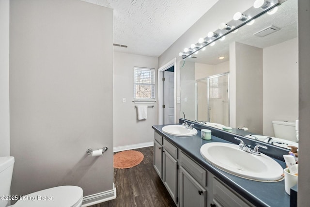 bathroom with wood-type flooring, a shower with door, toilet, a textured ceiling, and vanity