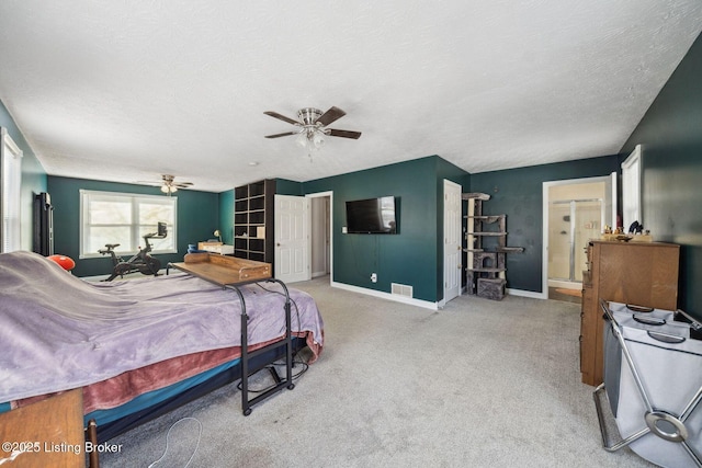 bedroom featuring ceiling fan, light colored carpet, a textured ceiling, and ensuite bath