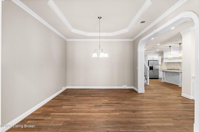 unfurnished dining area with an inviting chandelier, a tray ceiling, dark wood-type flooring, and crown molding