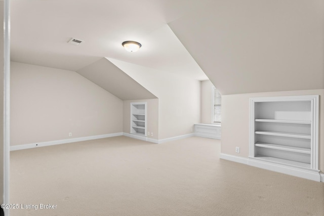 additional living space with vaulted ceiling, light colored carpet, and built in shelves